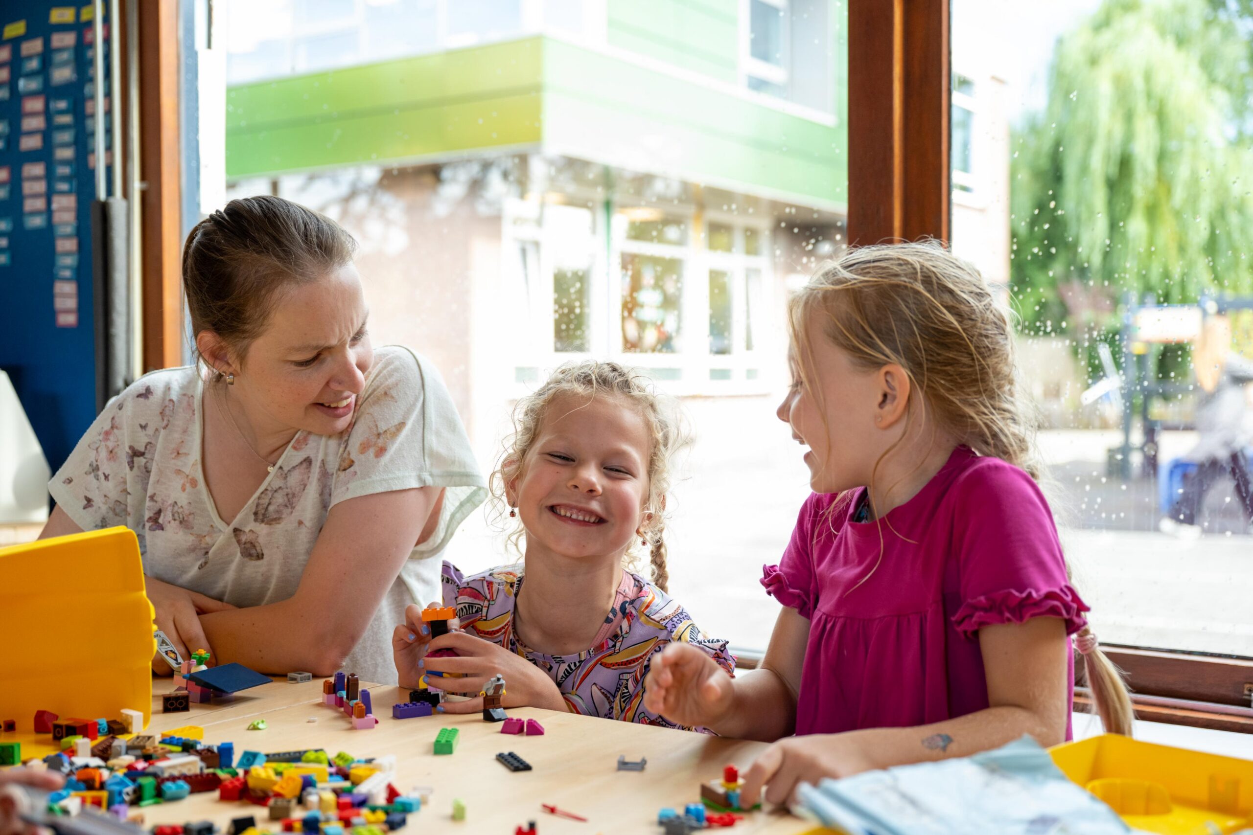 Twee meisjes en een pedagogisch medewerker moeten heel hard lachen terwijl ze een spelletje spelen